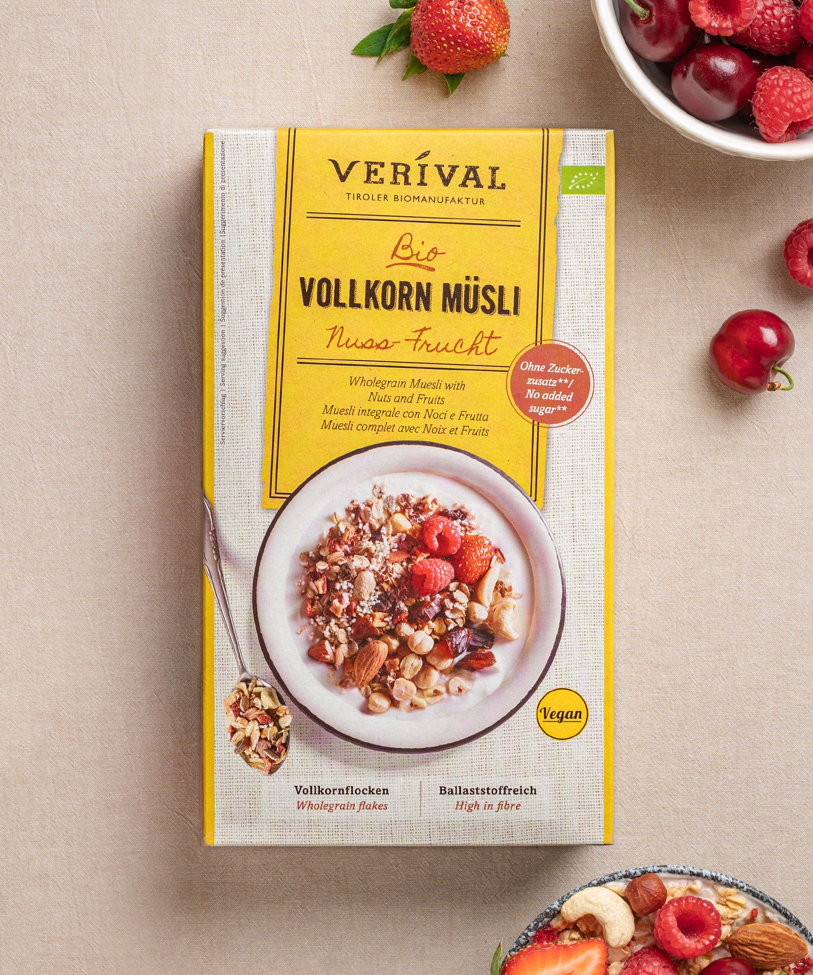 Eine Paket vom veganen Nuss-Frucht Vollkorn Müsli von Verival Bio steht mit gemischten Beeren und Körnern auf einem Tisch. Der hohe Ballaststoffgehalt und die Vollkorn-, Nuss- und Fruchtzutaten werden hervorgehoben.