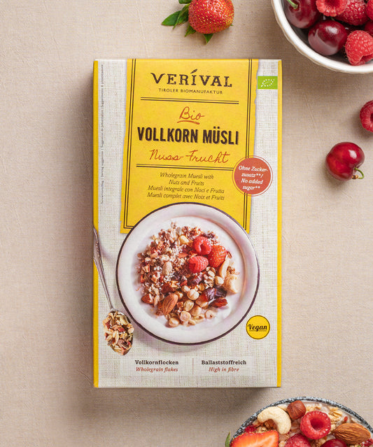 Eine Paket vom veganen Nuss-Frucht Vollkorn Müsli von Verival Bio steht mit gemischten Beeren und Körnern auf einem Tisch. Der hohe Ballaststoffgehalt und die Vollkorn-, Nuss- und Fruchtzutaten werden hervorgehoben.