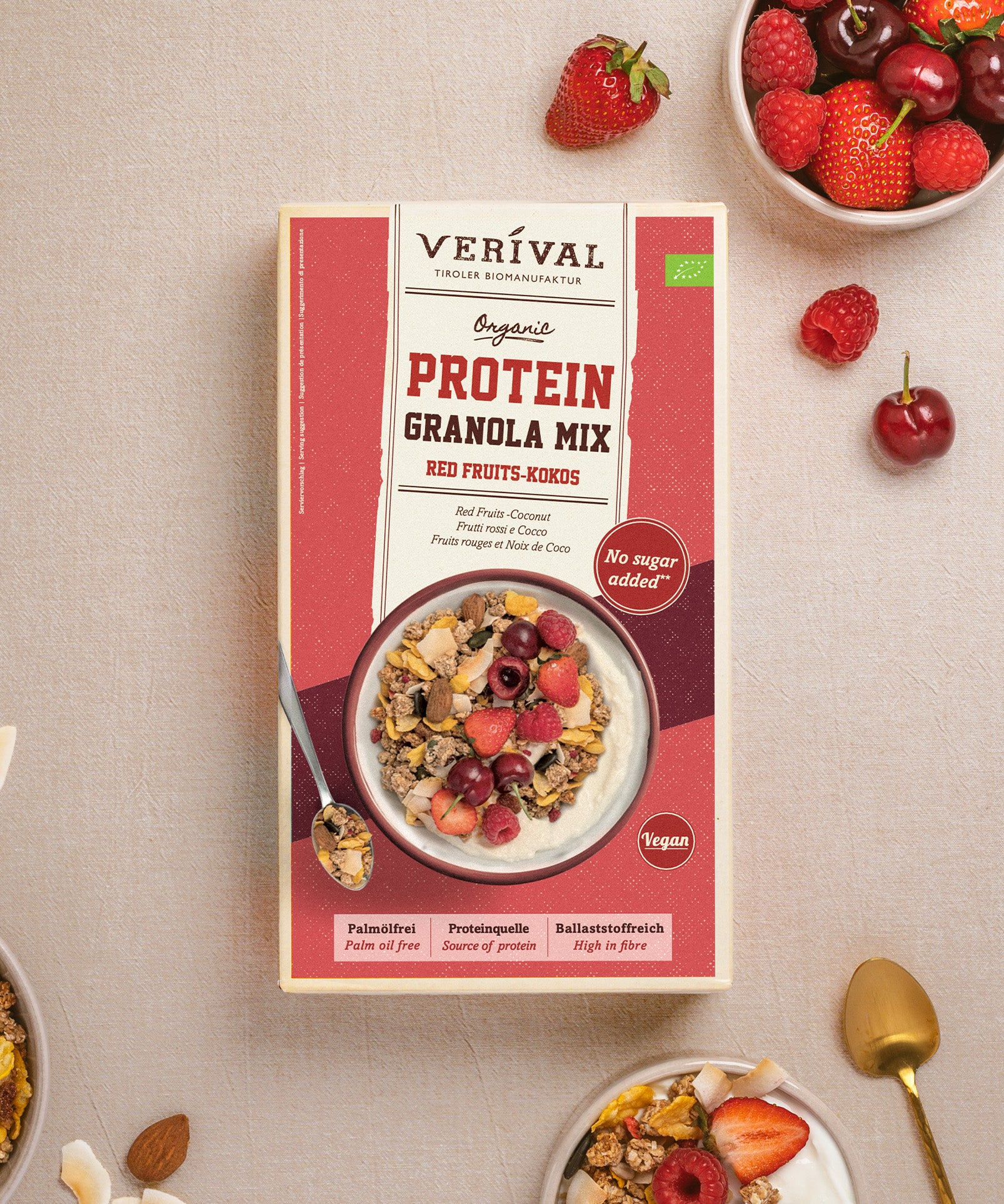 Das Bild zeigt ein Paket Protein Granola Mix Red Fruits-Kokos von Verival Bio neben frischen Beeren und einer Schüssel Granola und Milch.