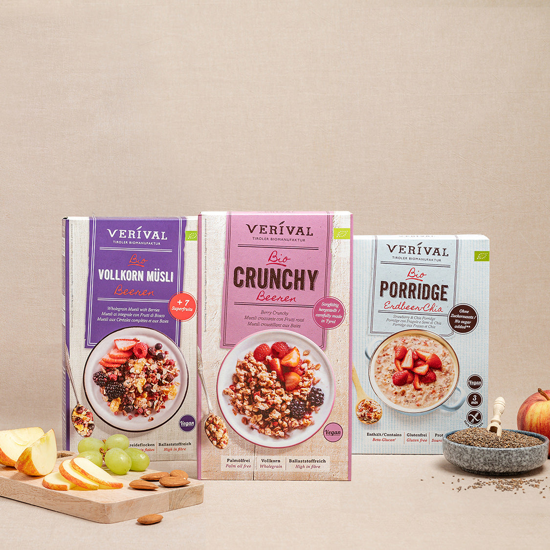 Tre scatole di prodotti muesli Verival (muesli integrale, frutti di bosco croccanti e porridge) sono presentate su uno sfondo neutro, con frutta e muesli davanti.