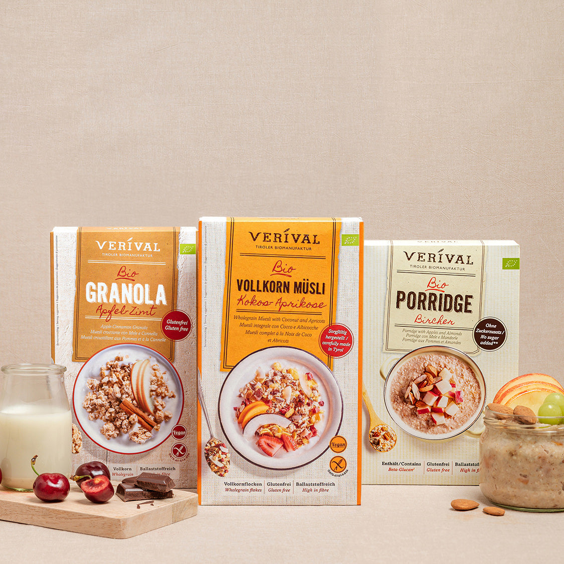Tre scatole di cereali etichettate Crunchy, Wholegrain Muesli e Porridge sono presentate con un bicchiere, ciliegie e mandorle su uno sfondo beige.