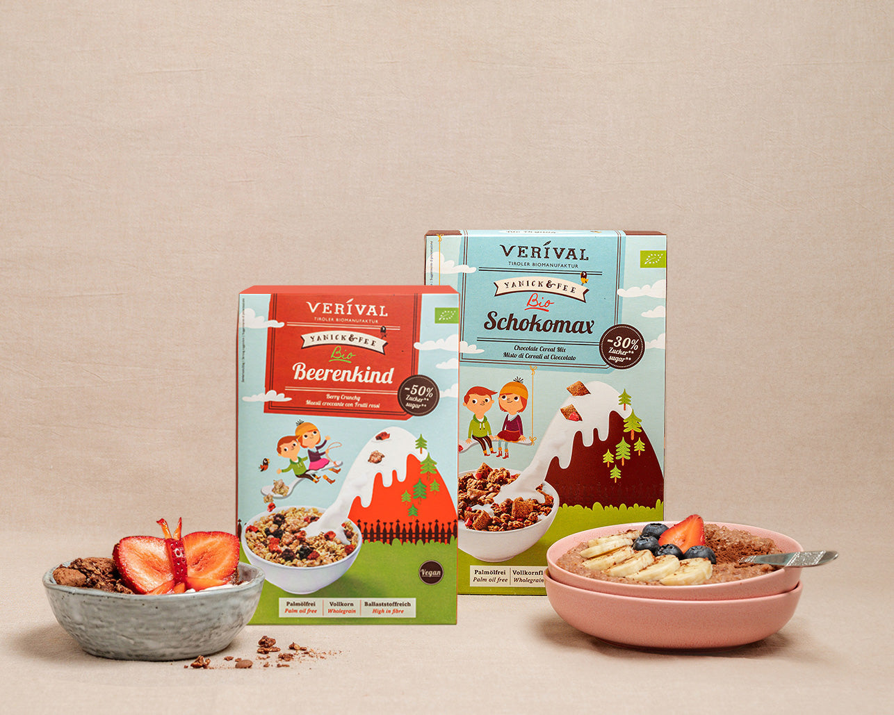 Dietro ciotole di muesli pronto, guarnite con frutta, su uno sfondo beige, si trovano due confezioni di muesli Verival.