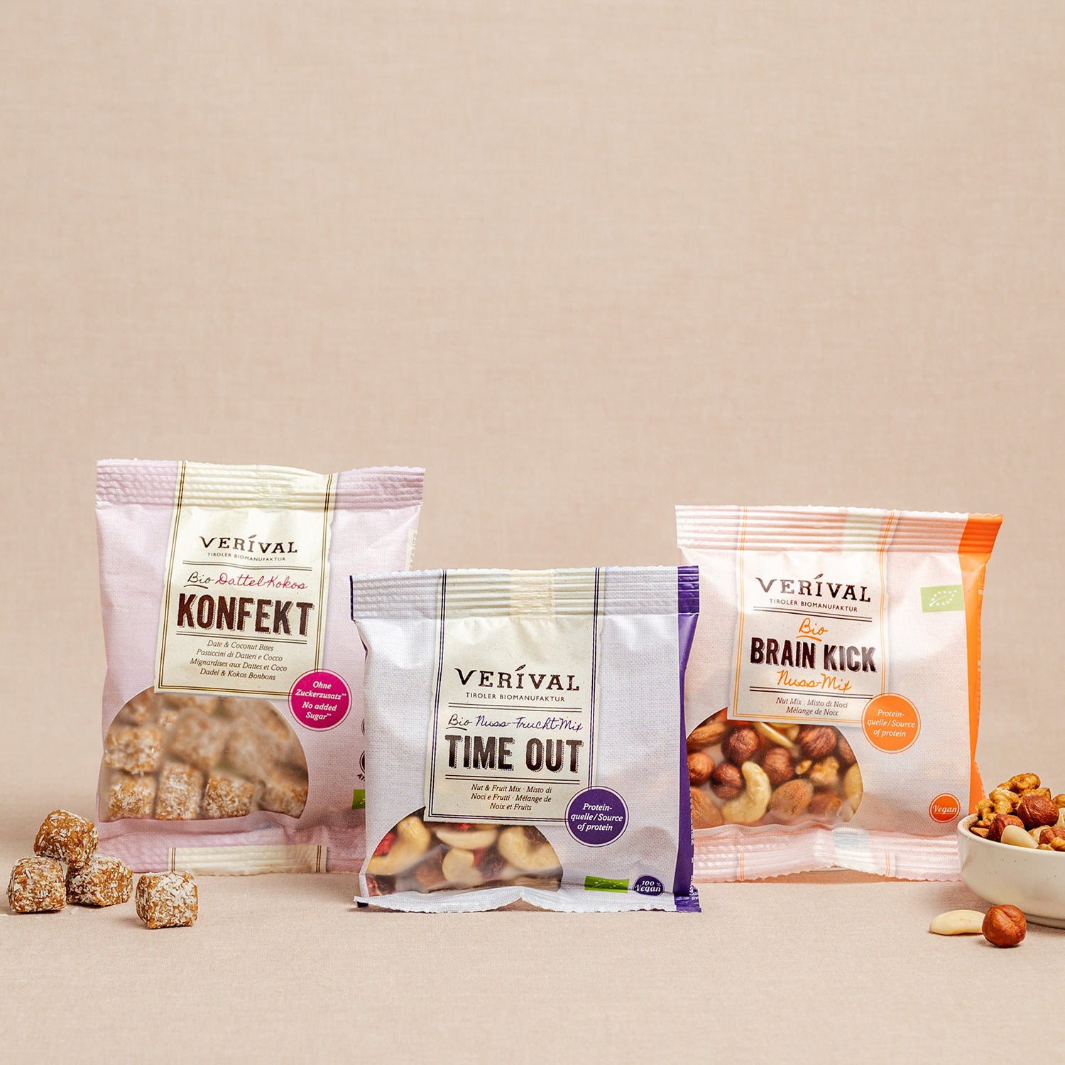 Tre confezioni di snack Verival – Konfekt, Time Out e Brain Kick – sono presentate in posizione verticale su una superficie neutra, con parte del contenuto sparso nelle vicinanze.