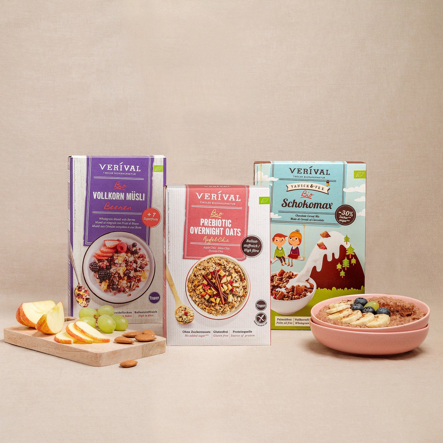 Sono esposte tre scatole di cereali Verival, tra cui muesli integrale, fiocchi d'avena prebiotici per la notte e Schokomax. Davanti a loro, una ciotola di muesli e frutta a fette su un tagliere.