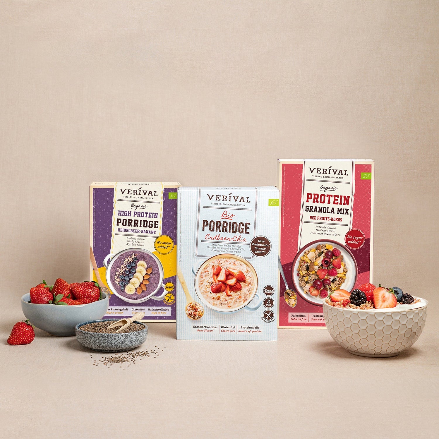 Sono esposte tre scatole di porridge e granola Verival, circondate da ciotole di frutti di bosco freschi e semi di chia su uno sfondo neutro.